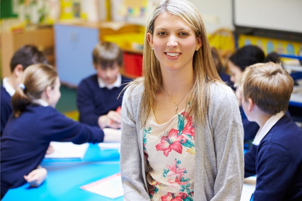 A female teacher smiling for a photograph with children behind her